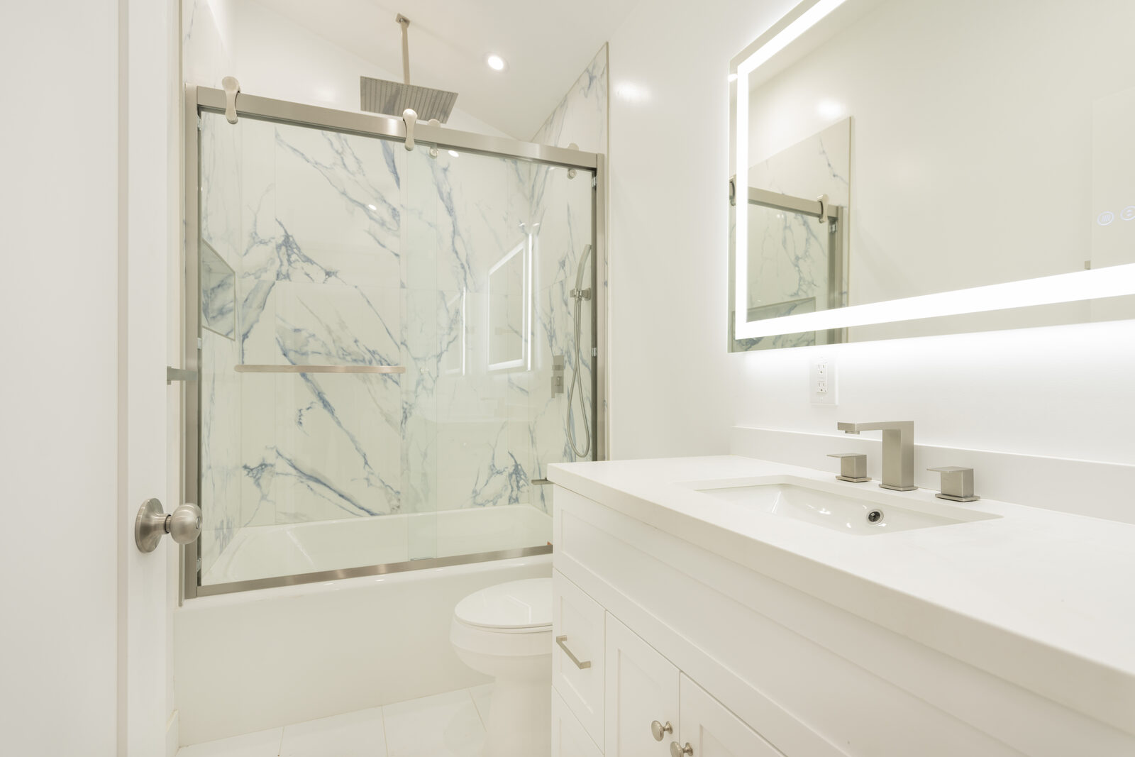 Bright bathroom with illuminated mirror, white vanity, and glass tub enclosure in the Thousand Oaks ADU