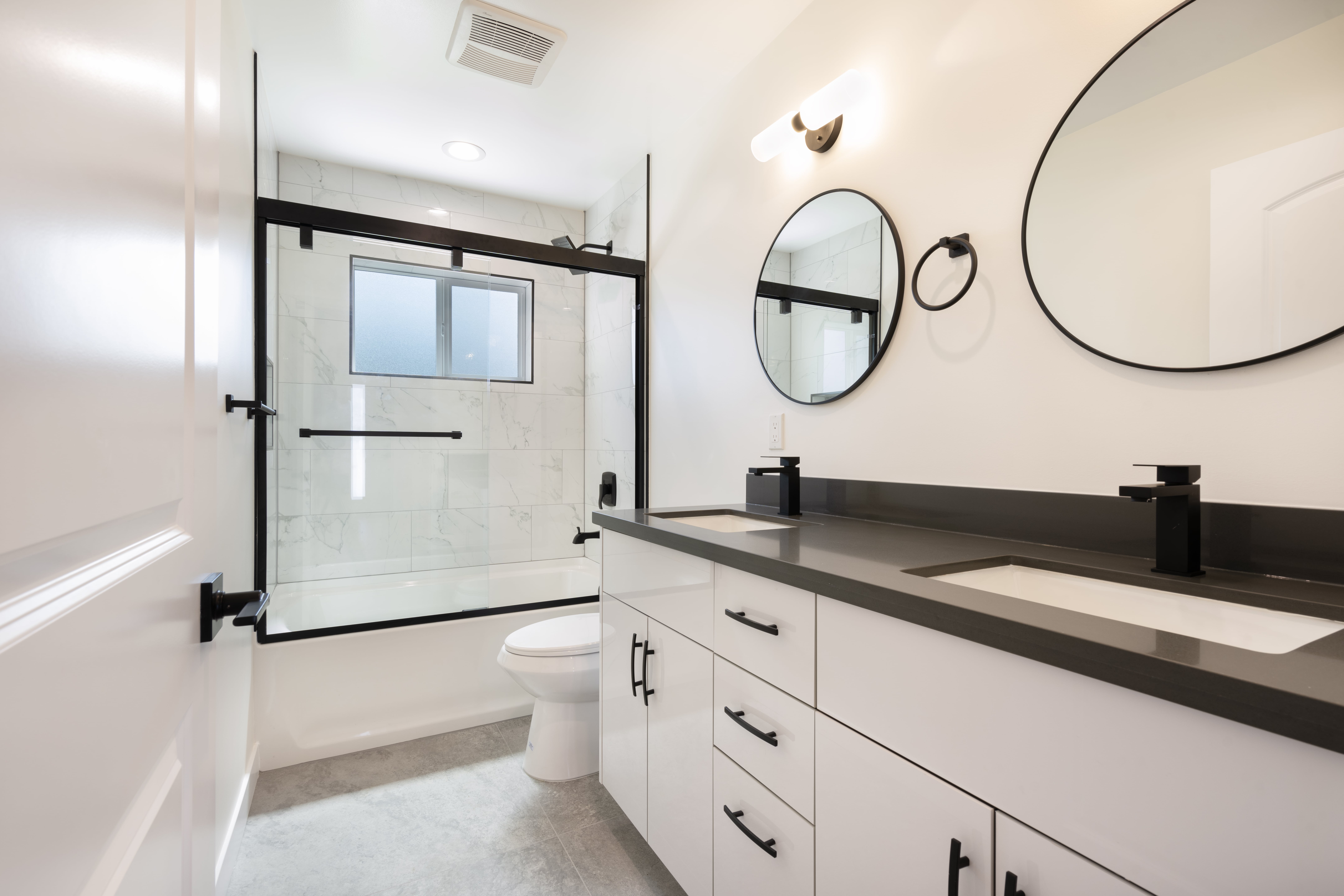 Luxury ADU bathroom with dual vanity, round mirrors, marble tile shower, and modern black fixtures