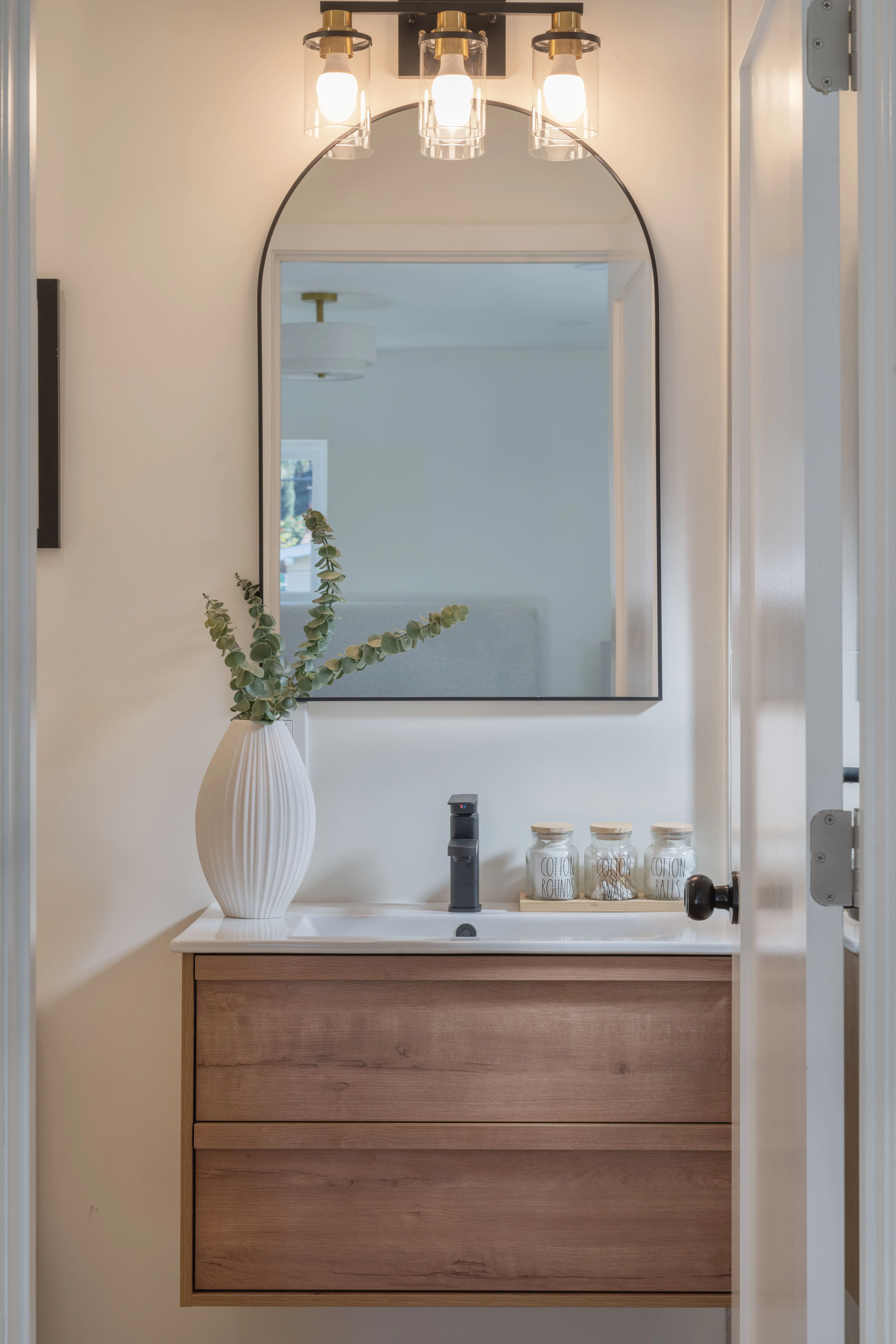 ADU bathroom vanity with floating oak cabinet, arched mirror, and modern black fixtures