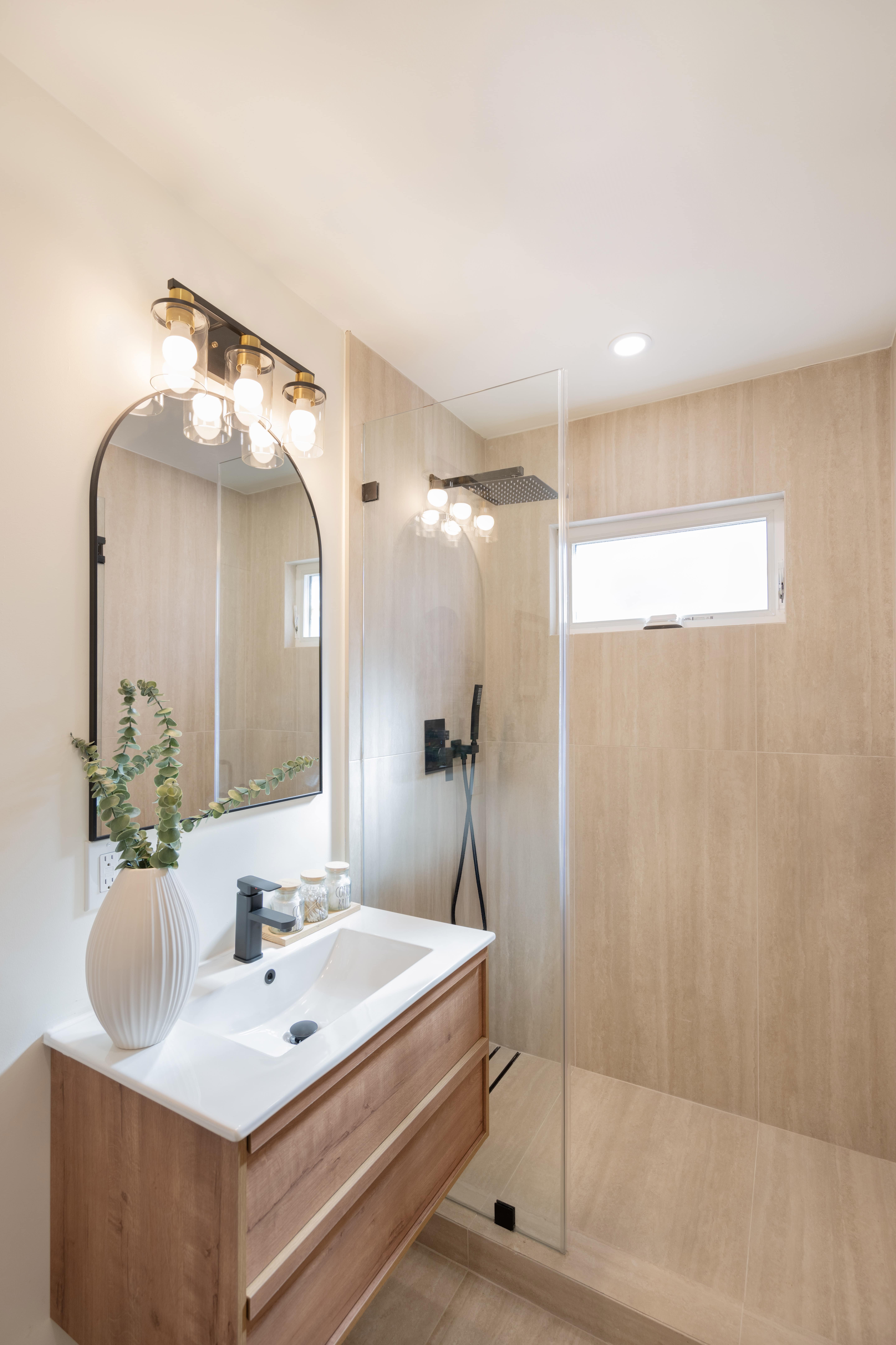 Modern ADU bathroom with floating oak vanity, rain shower head, glass enclosure, and natural stone tiles