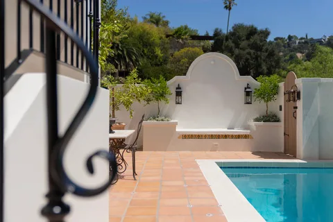 Terracotta courtyard beside a blue pool with a white stucco seating alcove