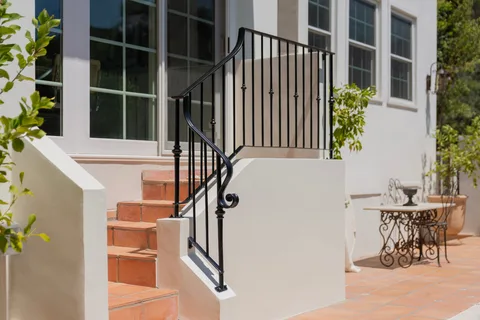 Terracotta entry steps with a curved black railing beside white stucco walls